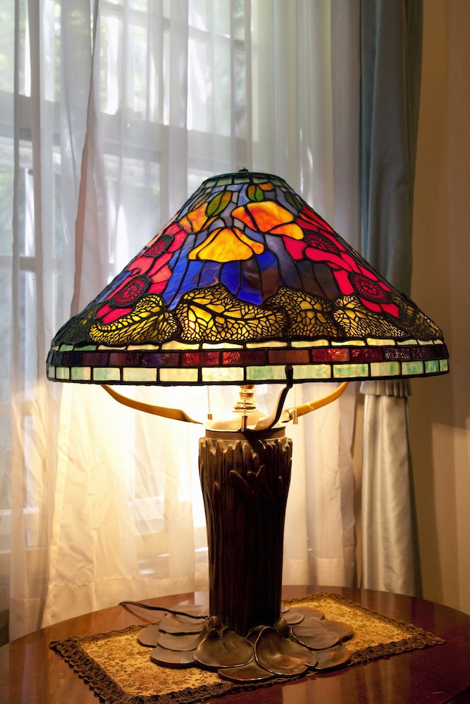 A stained glass lamp lit up in front of window.